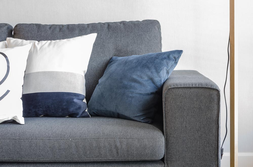 Dillerup Polsterreinigung – ein dunkeles Sofa mit weiß-blauen Kissen vor einer weißen Wand.